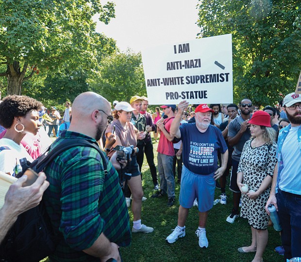 Counterprotesters surround Chris Willis, dressed in a T-shirt supporting President Trump and a cap bearing the Trump slogan “Make America Great Again,” as he holds up a sign supporting the Confederate statues.