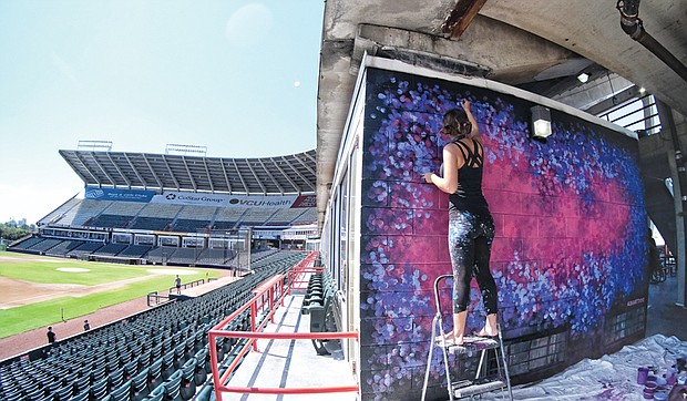 Shaylen Broughton paints an abstract of ruby reds and sapphire blues on a skybox wall.