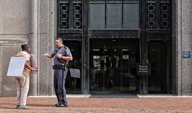 Beatrice Downs is confronted Friday by a Capitol Police officer as she pickets in front of the Patrick Henry Building in Capitol Square. She is told her demonstration on the state sidewalk is not allowed. 