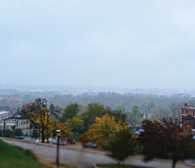 This rain-swept view from Libby Hill Park in the East End displays the bucolic side of Richmond. Instead of urban hustle and bustle, the scene shows a city engulfed in a soft fog that, with the hedge of colorful trees, obscures the view of the James River. Only an apartment building with an iconic smokestack provides a reminder of the crowded streets nearby. 
