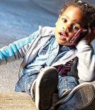 My’Isis Gee, 3, is content to talk with her dad on the cell phone Tuesday, while her mom, Michelle Gee, waits for the conversation to wrap up and the phone to be passed back. The Gees were in the 400 block of East Franklin Street in Downtown.