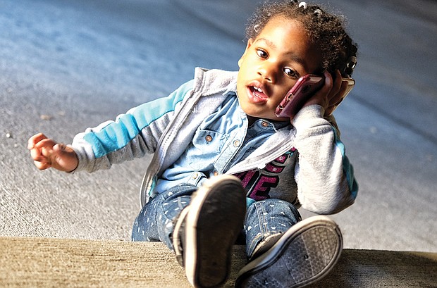 My’Isis Gee, 3, is content to talk with her dad on the cell phone Tuesday, while her mom, Michelle Gee, waits for the conversation to wrap up and the phone to be passed back. The Gees were in the 400 block of East Franklin Street in Downtown.