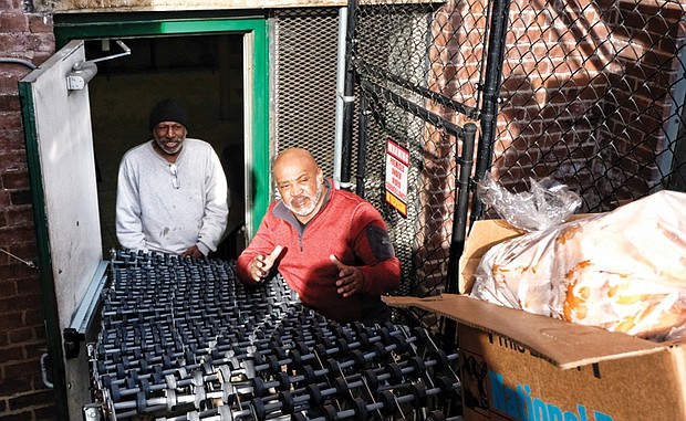 Bringing in the loaves //
Dr. Alonza L. Lawrence, right, pastor of Moore Street Missionary Baptist Church, and church member James Moses await a box filled with bread to make its way down a conveyor belt and into the church’s old social center on Monday morning. The two were helping to stock the food pantry at the Leigh Street church in the Carver neighborhood. The food delivery was from FeedMore, the hunger alleviation organization that serves Central Virginia. The church distributes free bags of groceries to all who stop by from 3 to 4 p.m. every Monday, except the next two — Christmas Day and New Year’s Day.