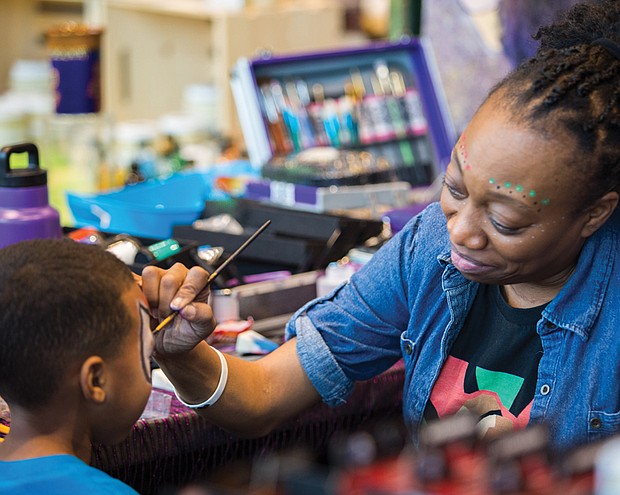 Kelita Wooten, bottom right, paints the face of a youngster during the festivities that included speakers, workshops and children’s activities.