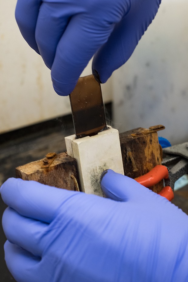 Robby Headrick uses a device built by his father, a woodworker, that holds one slide stable while the other is moved to create shear forces that align carbon nanotubes between them. The nanotubes form a film that can be peeled and rolled by hand to create short nanofibers for testing. (Credit: Jeff Fitlow/Rice University)