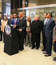 The Rev. A. Lincoln James Jr., pastor of Trinity Baptist Church, talks up his support for the meals tax at a City Hall press conference Tuesday. Mayor Levar M. Stoney, left, listens as 17 other ministers and Sheriff Antionette V. Irving, right, demonstrate the community support for his plan to generate money to build several new schools. 