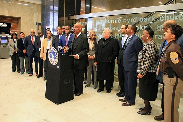 The Rev. A. Lincoln James Jr., pastor of Trinity Baptist Church, talks up his support for the meals tax at a City Hall press conference Tuesday. Mayor Levar M. Stoney, left, listens as 17 other ministers and Sheriff Antionette V. Irving, right, demonstrate the community support for his plan to generate money to build several new schools. 