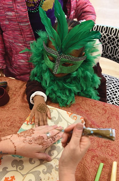 After donning a mask and feather boa, 4-year-old Marshall Howard gets a henna tattoo during the main event inside the center on West 15th Street. Music, performances by several groups and Cajun-style food were featured, along with a King Cake.