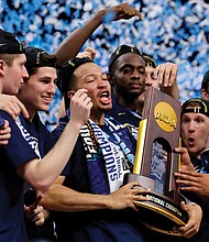 Villanova University’s Jalen Brunson, center, holds the championship trophy with teammates after beating the University of Michigan 79-62 on Monday to win the NCAA men’s title.