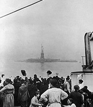 In this undated historical photo, a group of immigrants traveling aboard a ship celebrate as they catch their first glimpse of the Statue of Liberty and Ellis Island in New York Harbor.