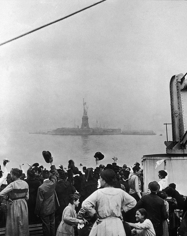 In this undated historical photo, a group of immigrants traveling aboard a ship celebrate as they catch their first glimpse of the Statue of Liberty and Ellis Island in New York Harbor.