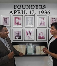 Randy N. Cooper, president and chief executive officer of Richmond Heritage Federal Credit Union, proudly shows off to his wife, Shirley G. Cooper, a wall display at the credit union's Commerce Road branch celebrating its founders. Mrs. Cooper is president and chief executive officer of the Credit Union of Richmond.