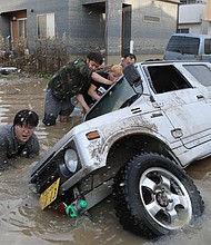 Residents try to upright a vehicle stuck in a flood hit area in Kurashiki, Okayama prefecture on July 9, 2018.Residents try to upright a vehicle stuck in a flood hit area in Kurashiki, Okayama prefecture on July 9, 2018.