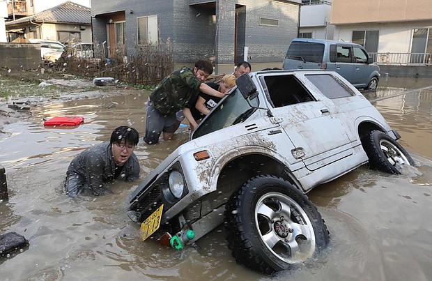 Residents try to upright a vehicle stuck in a flood hit area in Kurashiki, Okayama prefecture on July 9, 2018.Residents try to upright a vehicle stuck in a flood hit area in Kurashiki, Okayama prefecture on July 9, 2018.