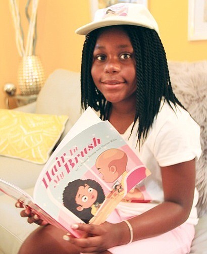 Taylor Ellis, 10, author of “Hair in My Brush” reviews a  copy of her book about a young African-American girl who is diagnosed with alopecia.