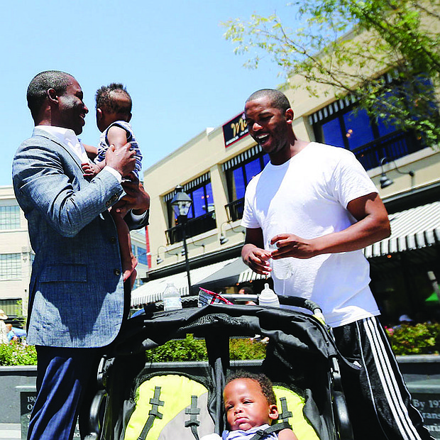 CELEBRATING A RICHMOND ICON-Richmond Mayor Levar M. Stoney holds 10-month-old Nasir Jackson while the infant’s dad, Timothy Jackson, and twin brother, Dakari, pause beside the statue of Richmond businesswoman Maggie L. Walker during Saturday’s celebration Downtown honoring her 154th birthday.