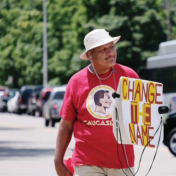 Hundreds of fans and autograph seekers flocked to the Washington professional football team’s training field to hobnob with their favorite players during last Saturday’s Fan Appreciation Day. Outside the gate, Stephen Rivera of Richmond protests the team’s racist name and mascot, which are offensive to many Native Americans.