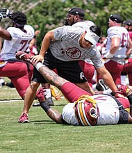 Hundreds of fans and autograph seekers flocked to the Washington professional football team’s training field to hobnob with their favorite players during last Saturday’s Fan Appreciation Day. Pictured here, a trainer works with a player on stretches, an important part of the practice session.