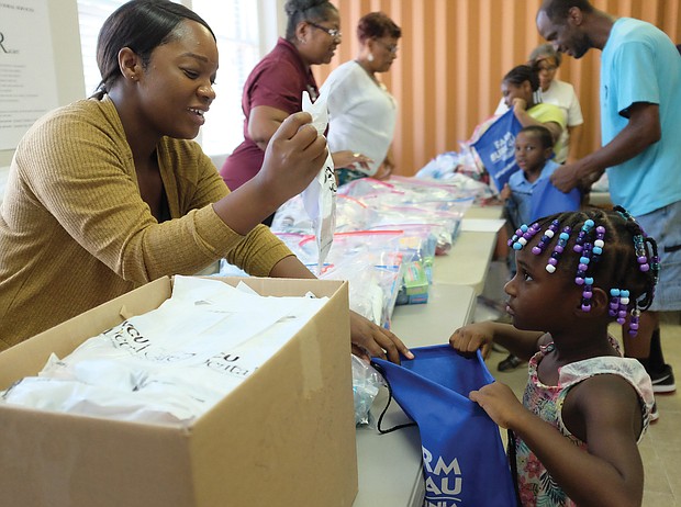 Volunteer Latisha Gordon gives school supplies and other goodies to 4-year-old Jayla Morrison at the Richmond Police Athletic League’s Stop the Violence rally last Sunday at Lucks Field in the East End. The event, with free food, beverages and music, was organized to help bridge the gap between Richmond Police and the community, while also helping youngsters get ready for school.