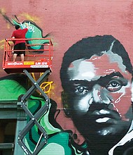 A new mural featuring Richmond newspaper great John Mitchell Jr. is the latest work of the 26-year-old artist known as “Visibly Hidden.” Here, the artist, also known as George Fernandez, signs his name on the giant painting that faces the Maggie L. Walker Statue at Broad and Adams streets. Location: 100 W. Broad St. (Regina H. Boone/Richmond Free Press)