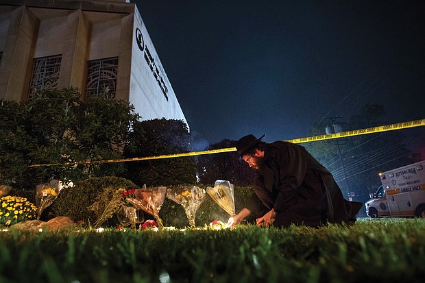 Rabbi Eli Wilansky lights a candle outside the Tree of Life Synagogue in Pittsburgh’s Squirrel Hill neighborhood on Saturday night following a deadly mass shooting at the temple. Memorial flowers and candles lined the site, despite the yellow police crime scene tape.