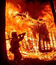 Firefighter Jose Corona sprays water as flames consume a home in Magalia, California