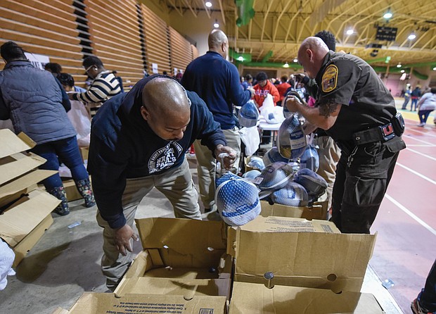 Thanksgiving comes early: Dozens of people wait in line in the rain last Thursday outside the Arthur Ashe Jr. Athletic Center in Richmond to receive boxed Thanksgiving meals. The Thanksgiving Harvest food program was sponsored by St. Paul’s Baptist Church and a coalition of Richmond area organizations. Inside the Ashe Center, Jason Worrell, left, and Sgt. Jeff Owen with the Richmond Sheriff’s Office help distribute turkeys to the more than 2,000 families that came through the line. (Photos by Clement Britt)