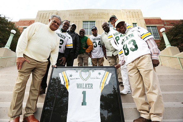 Members of the 1975 undefeated football team at Maggie L. Walker High School stand Monday on the steps of their alma mater holding a commemorative jersey they plan to present to the school. They are, from left, former Coach Richard McFee; running back Jeff Washington; flanker Richard Thomas; return specialist Richard Stuart; fullback William Washington; middle linebacker Mike Liggans; wide receiver Pierre Johnson; and former athletic director Howard Hopkins.