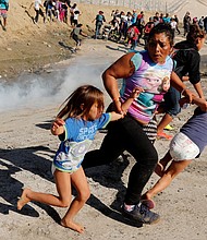 A migrant family runs from tear gas released by US border patrol agents near the fence between Tijuana, Mexico, and San Diego.