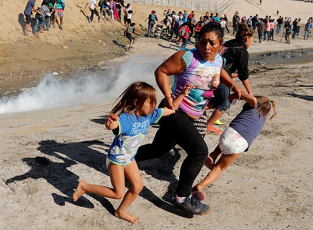 A migrant family runs from tear gas released by US border patrol agents near the fence between Tijuana, Mexico, and San Diego.