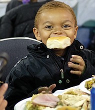 Delicious! Jabriel Birchett, 5, takes a bite of his roll on Thanksgiving Day and doesn’t want to let go. The youngster was enjoying good food with family at The Giving Heart Community Thanksgiving Feast at the Greater Richmond Convention Center in Downtown. (Sandra Sellars/Richmond Free Press)