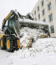 Brrrrr! The first snowfall of the season last Sunday resulted in people heading outdoors in the cold to clear snowy walkways and parking spots so that people and cars could safely maneuver. A snow plow removes several inches of snow covering the parking lot of the Virginia Housing Development Authority at 601 S. Belvidere St. (Sandra Sellars/Richmond Free Press)