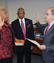 Richmond School Board member Cheryl L. Burke takes the oath of office Tuesday at City Hall while her husband, Emmitt Burke, holds the Bible. Administering the oath of office is Richmond Circuit Court Clerk Edward F. Jewett.