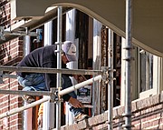 A worker paints windows last Saturday on the former Fulton Elementary School property that is being renovated into 33 apartments in the city’s East End. (Sandra Sellars/Richmond Free Press)