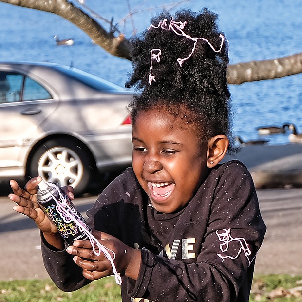 Warming up to winter: Chelsea Garba, 5, gets carried away with a spray can of Goofy String while playing with her dad, Makka Garba, by Fountain Lake in Byrd Park last Saturday, when the day was sunny and temperatures hovered near 60 degrees. What a change this weekend will bring, when high temperatures will be in the 30s, with snow forecast for Sunday. (Sandra Sellars/Richmond Free Press)