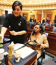 New year, new session: Delegate Hala S. Ayala of Prince William County adjusts a yellow rose — representing support for the ERA — on the desk of a Prince William colleague, Delegate Jennifer D. Carroll Foy. (Regina H. Boone/Richmond Free Press)