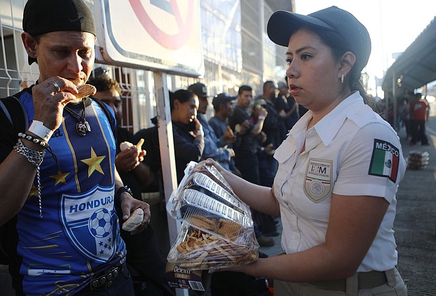Central American migrants, part of a new 'migrant caravan', are given food by a Mexican immigration official while standing on the international border bridge between Guatemala and Mexico to wait for humanitarian visas on January 18, 2019 in Ciudad Hidalgo, Mexico