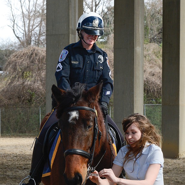 Whoa, Aslan!-Tori Branard makes a final adjustment to Aslan’s bridle at the Feb. 7 badging ceremony inducting the horse into the Richmond Police Department’s Mounted Unit. As a student at Asbury University’s unique Service Mounts Program in Kentucky, Ms. Branard spent three years training Aslan, a Percheron-thoroughbred cross. Watching is Aslan’s amused partner, Master Patrol Officer Amanda Acuff. Aslan is the fourth horse in the unit and is a replacement for Rio, who was retired in December. The others are Samson, Scooter and Toby. The horses live in a condemned stable near Gilpin Court. The police department is seeking other sources of funding for a new facility after recent bids to replace the current stable came in $1 million over budget. (Clement Britt)