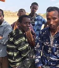 A group of men wait for smugglers to arrive to take them across the Bab al-Mandeb Strait to Yemen.