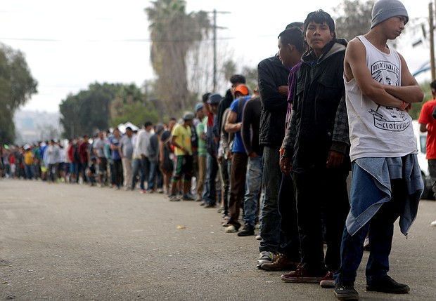 Members of the 'migrant caravan' wait in line to receive breakfast outside a temporary shelter set up for members of the caravan on November 24, 2018 in Tijuana, Mexico.