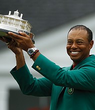 Tiger Woods holds the championship trophy wearing the green jacket donned by winners after coming from behind to claim victory Sunday at the Masters Tournament in Augusta, Ga.