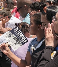 A member of the crowd cools herself with a souvenir fan in the morning heat at last Saturday’s unveiling ceremony. (Ava Reaves/Richmond Free Press)