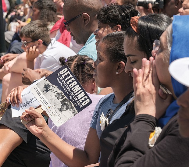 A member of the crowd cools herself with a souvenir fan in the morning heat at last Saturday’s unveiling ceremony. (Ava Reaves/Richmond Free Press)