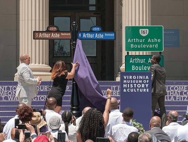 Richmond City Councilwoman Kim B. Gray, 2nd District, pulls down the last curtain to unveil the new Arthur Ashe Boulevard signs as Mr. Ashe’s nephew, David O. Harris Jr., left, and Mayor Levar M. Stoney watch.  (Ava Reaves/Richmond Free Press)