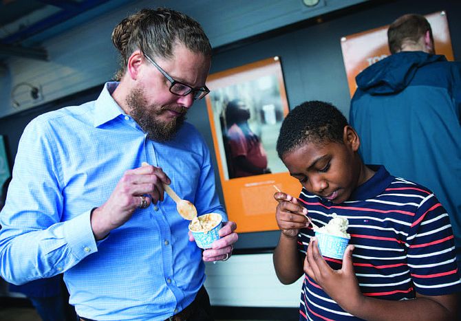 Ben & Jerry’s CEO Matthew McCarthy and Rasir Corzen, 11, of Philadelphia, Pa., enjoy ice cream while viewing the newly opened Art for Justice exhibit at the Ben & Jerry’s factory on Tuesday, June 25, 2019 in Waterbury, Vt. The exhibit highlights the need for criminal justice reform and features artwork by formerly-incarcerated artists. (Andy Duback/AP Images for Ben & Jerry’s)
