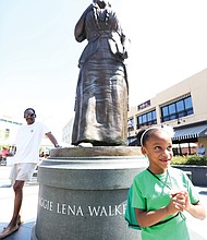 Lyla Hopkins-Hawkins, 6, stands at the foot of the statue of noted Richmond businesswoman and activist Maggie L. Walker at Broad and Adams streets in Downtown during last Saturday’s commemoration of Mrs. Walker’s 155th birthday. The young- ster attended the event with her grandfather, J. Maurice Hopkins, a 1965 graduate of Maggie L. Walker High School who helped push the effort to erect the statue. Also attending the event is Dr. Johnny Mickens III, left, Mrs. Walker’s great-grandson. (Regina H. Boone/Richmond Free Press)