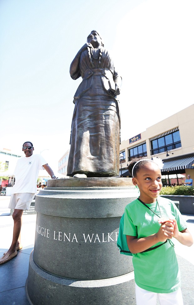 Lyla Hopkins-Hawkins, 6, stands at the foot of the statue of noted Richmond businesswoman and activist Maggie L. Walker at Broad and Adams streets in Downtown during last Saturday’s commemoration of Mrs. Walker’s 155th birthday. The young- ster attended the event with her grandfather, J. Maurice Hopkins, a 1965 graduate of Maggie L. Walker High School who helped push the effort to erect the statue. Also attending the event is Dr. Johnny Mickens III, left, Mrs. Walker’s great-grandson. (Regina H. Boone/Richmond Free Press)