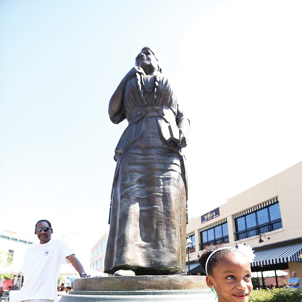 Lyla Hopkins-Hawkins, 6, stands at the foot of the statue of noted Richmond businesswoman and activist Maggie L. Walker at Broad and Adams streets in Downtown during last Saturday’s commemoration of Mrs. Walker’s 155th birthday. The young- ster attended the event with her grandfather, J. Maurice Hopkins, a 1965 graduate of Maggie L. Walker High School who helped push the effort to erect the statue. Also attending the event is Dr. Johnny Mickens III, left, Mrs. Walker’s great-grandson. (Regina H. Boone/Richmond Free Press)