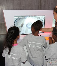 Power Scholars Academy students and a YMCA instructor look at a security camera’s view of the lobby at one of the Science Museum’s technology exhibits.