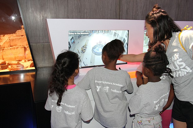 Power Scholars Academy students and a YMCA instructor look at a security camera’s view of the lobby at one of the Science Museum’s technology exhibits.